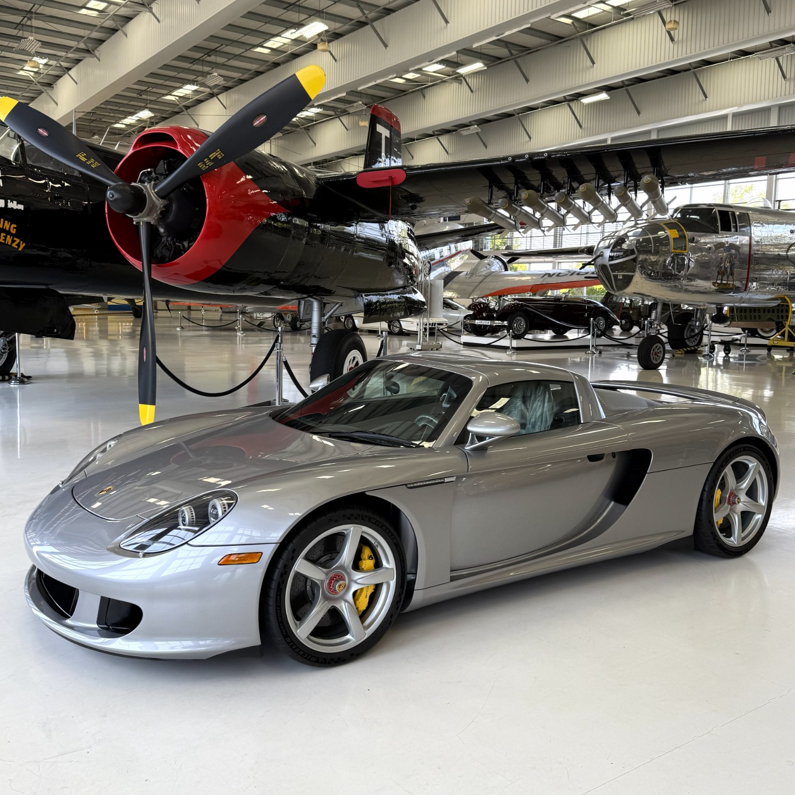 A silver Porsche Carrera GT among vintage warbirds in a private hangar